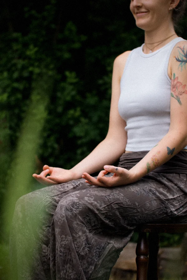 Eine Frau sitzt aufrecht in Meditation auf einem Stuhl im Freien als Beispiel für Senioren-Yoga bei Sonnenkind Yoga.