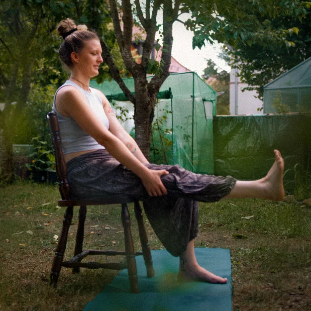 Madeleine Zimmer praktiziert Stuhl-Yoga im Garten mit einer sanften Beinstreckung für den Senioren-Yoga-Kurs.