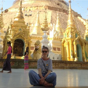 Madeleine Zimmer sitzt entspannt im Schneidersitz vor einer prachtvollen goldenen Pagode während ihrer spirituellen Reise.