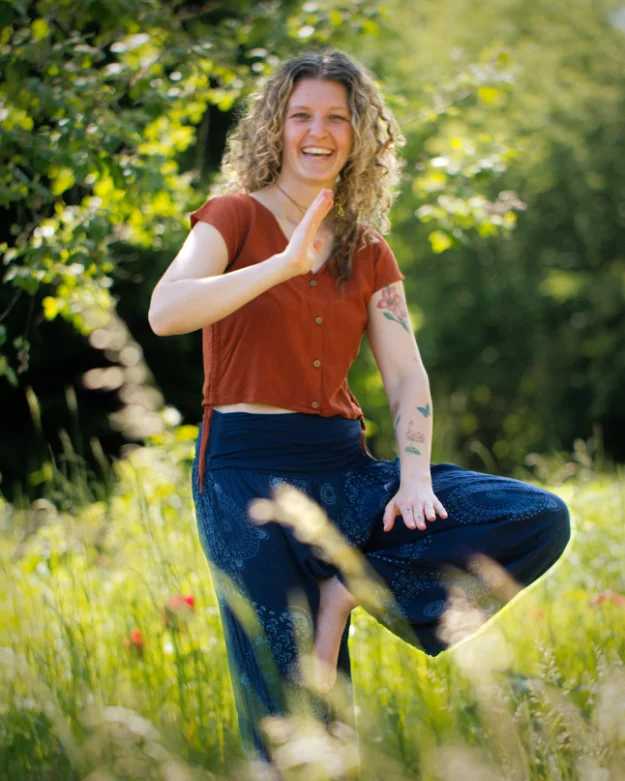 Die lachende Yoga-Lehrerin Madeleine Zimmer von Sonnenkind Yoga praktiziert die Baum-Pose auf einer sonnigen Sommerwiese.