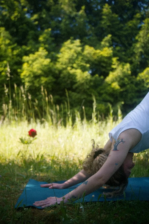 Eine Frau praktiziert den herabschauenden Hund auf einer blauen Yogamatte auf einer sonnigen Blumenwiese für bewusste Kräftigung und Dehnung.