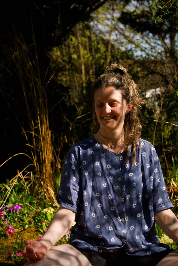 Yogalehrerin Madeleine Zimmer sitzt lächelnd im Meditationssitz in der Natur für ein bewusstes Spüren im Unterricht.